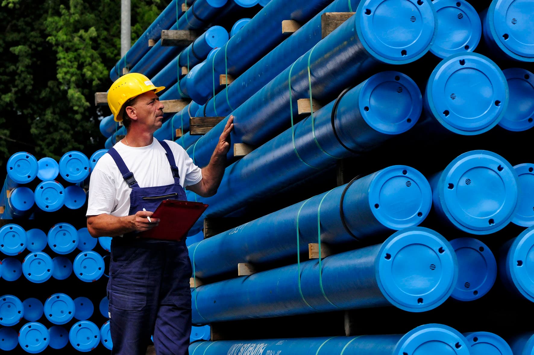 Mann mit Bauhelm kontrolliert im Rohrlager blaue Wasserrohre.
